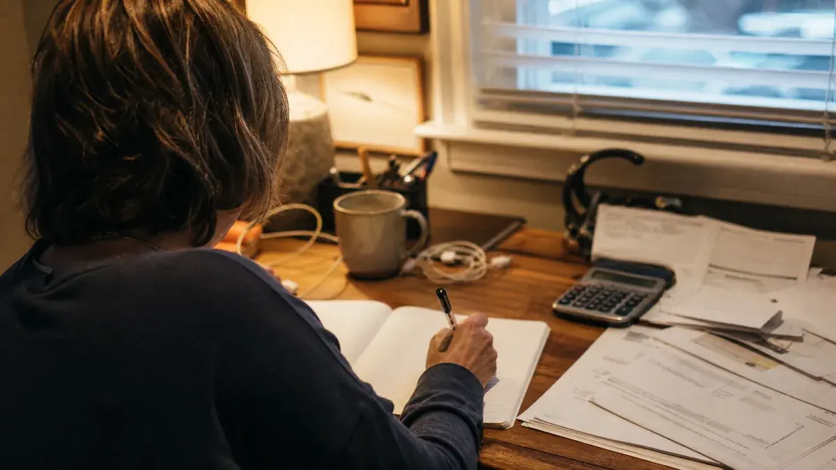 Coral Jacobs working through a household budget by hand at a desk